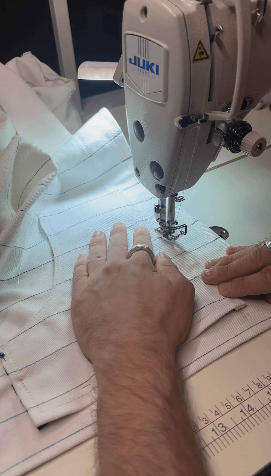 Person sewing fabric with a Juki industrial sewing machine, hands guiding material, ruler nearby, workspace well-lit.