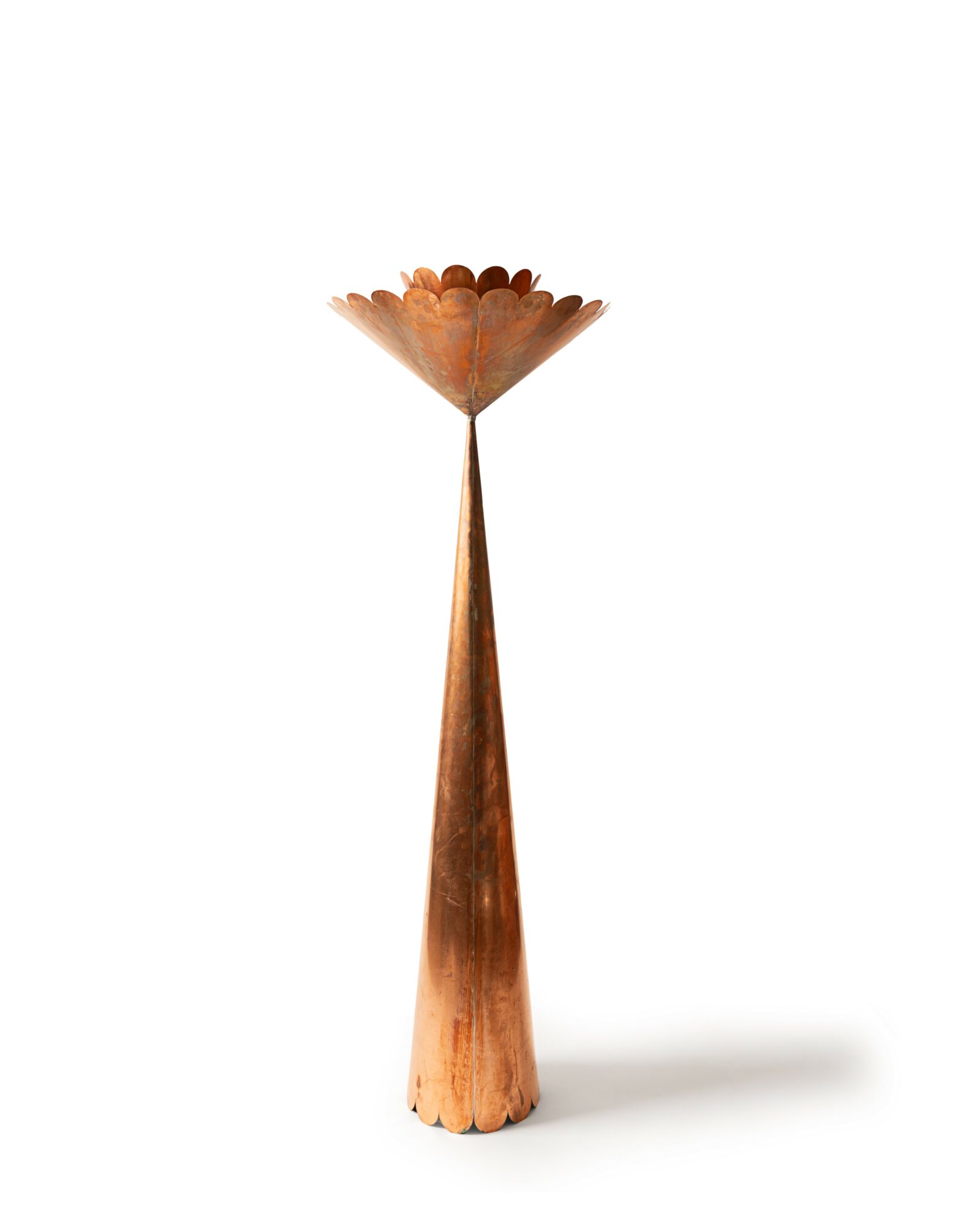 A copper-colored, cone-shaped object with a scalloped edge at the top, standing upright on a white background.