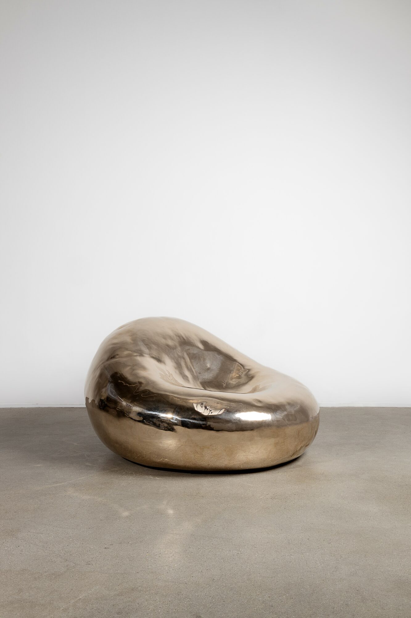 Shiny metallic abstract sculpture on a concrete surface against a plain white background.