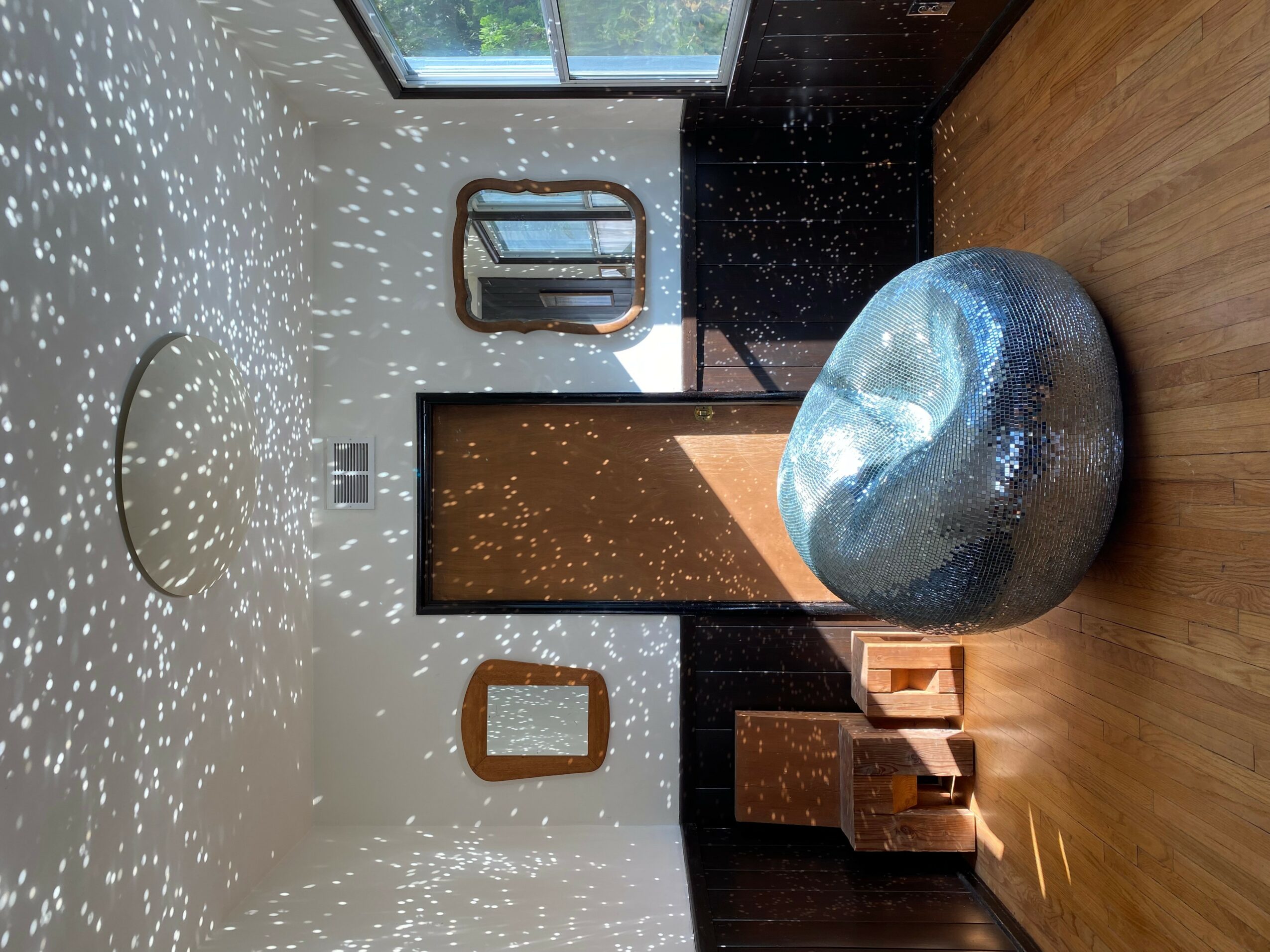 Room with a window, mirror, and a large round textured object on a wooden floor, with light reflections on the ceiling.