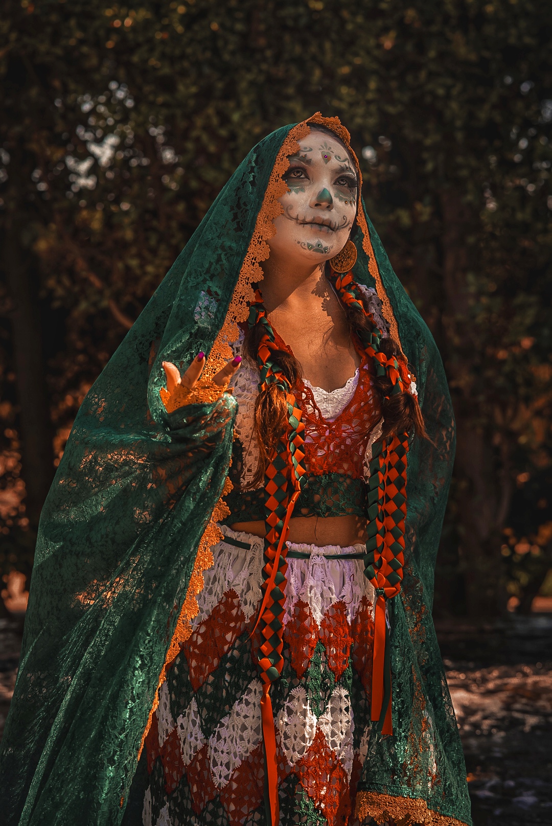 Person dressed in colorful costume with face paint, wearing a green veil, standing outdoors at night.