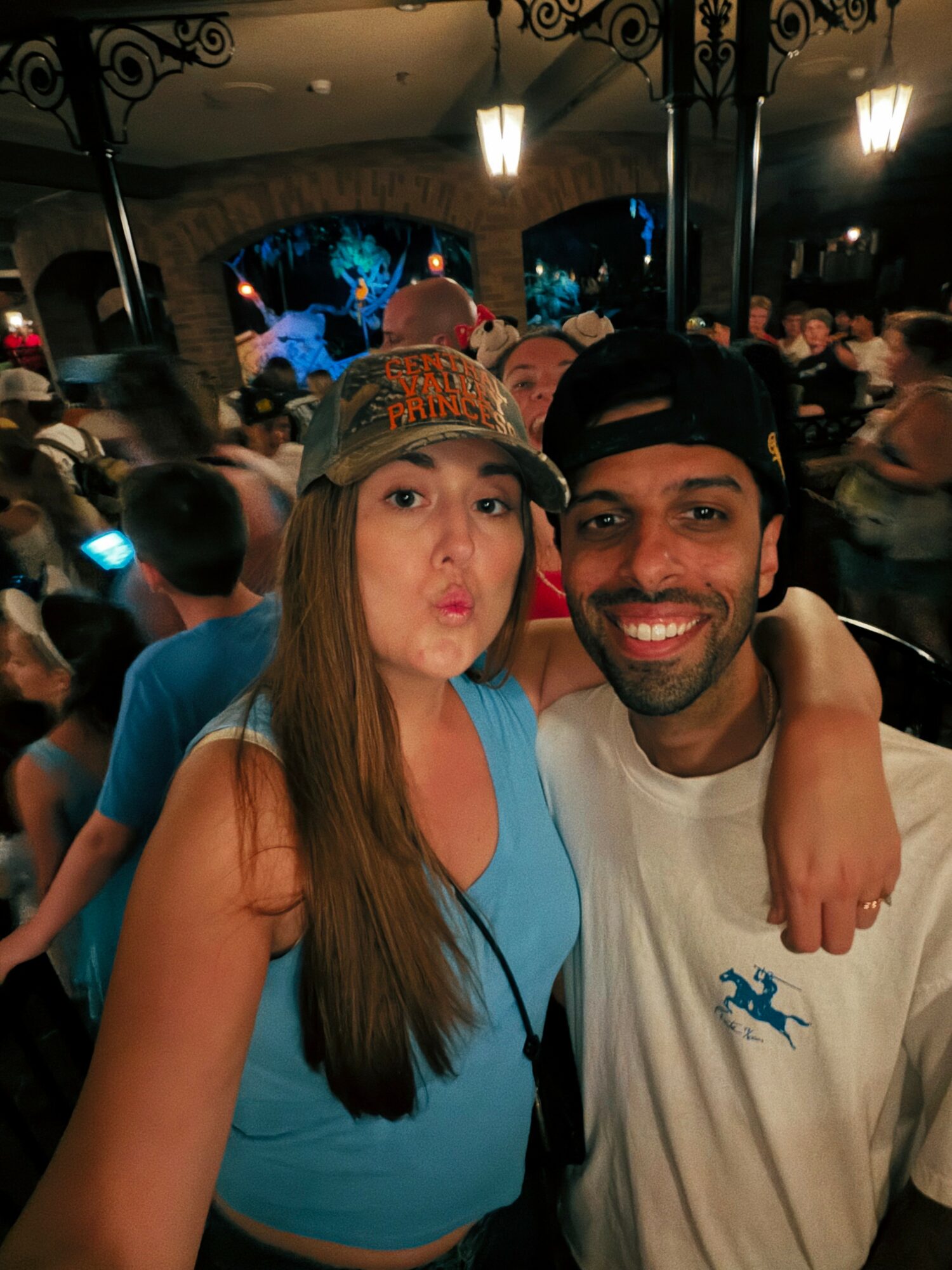 Two people smiling and posing for a photo in a crowded indoor setting at night.